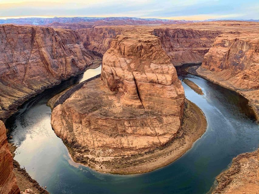 A wide river winds in a horseshoe shape around a massive red rock formation within a deep canyon.
