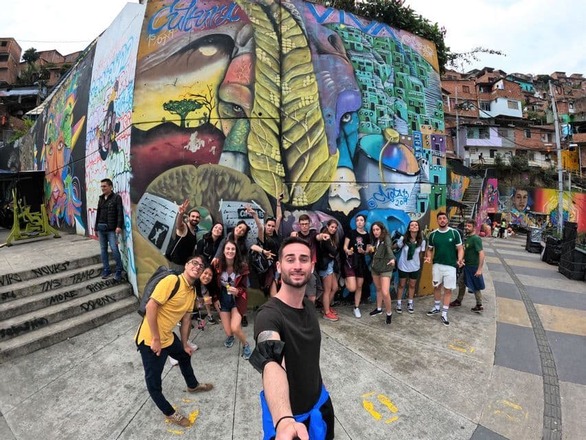 Un grupo de WeRoad posa para una selfie frente a un enorme mural de grafiti colorido en un barrio en la ladera.