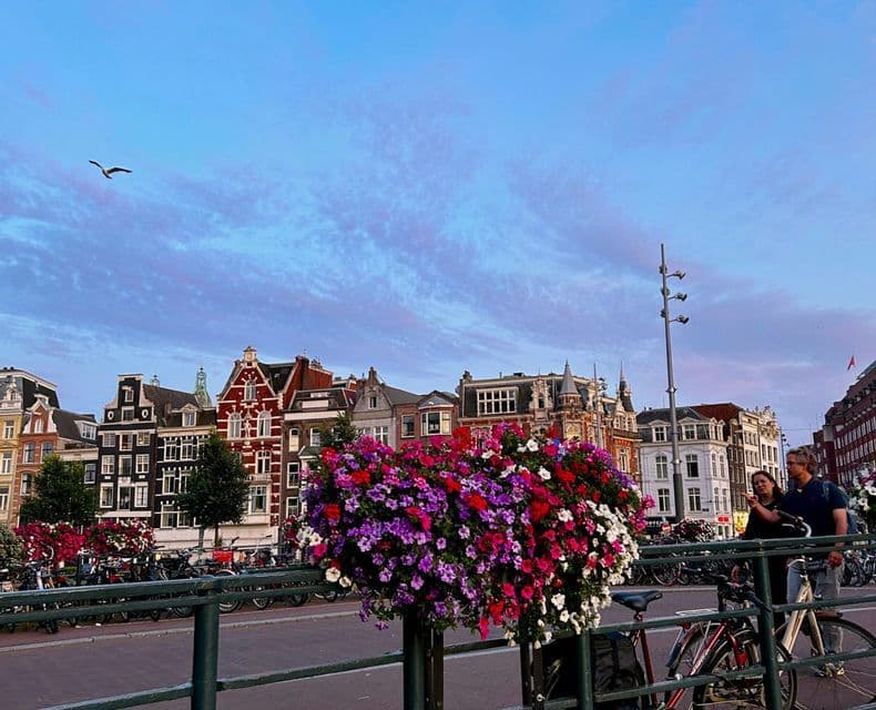 Flores coloridas en una maceta colgante en un puente con vistas a una calle con casas tradicionales de tejado a dos aguas al atardecer.