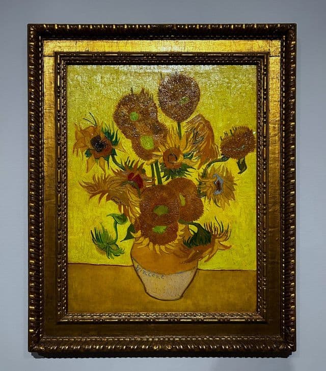 Le tableau 'Les Tournesols' de Vincent van Gogh dans un cadre orné et doré, accroché au mur d'une galerie.