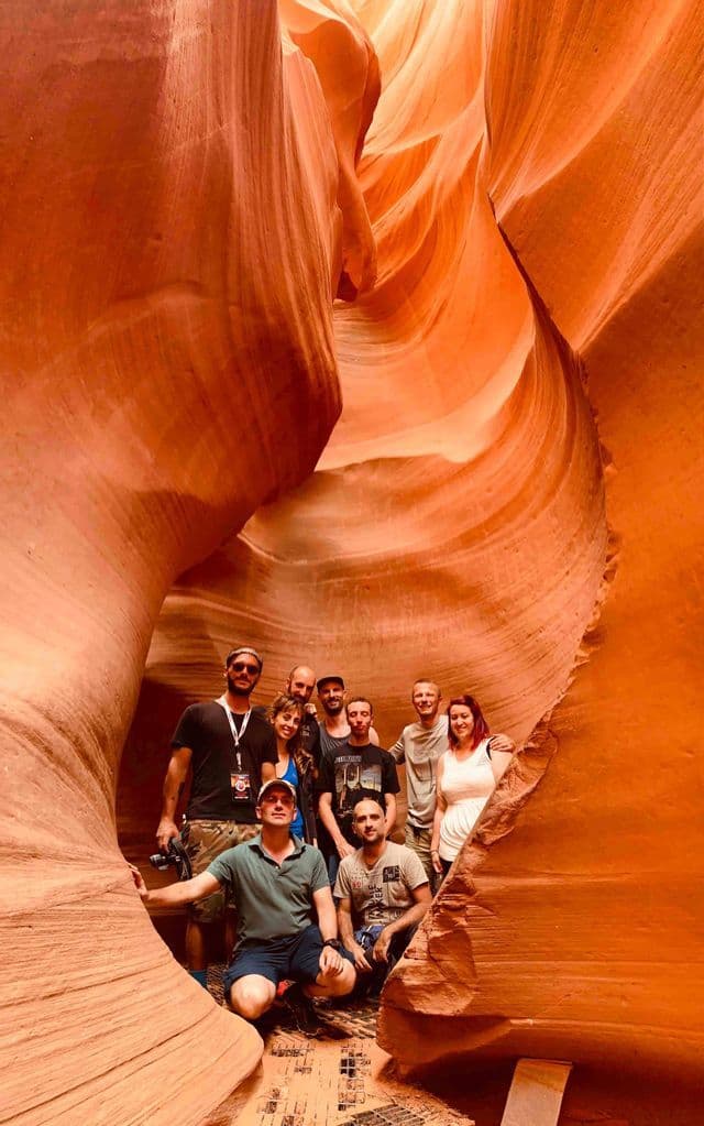 A WeRoad group trip posing for a photo together inside a narrow slot canyon with orange, wavy rock formations.