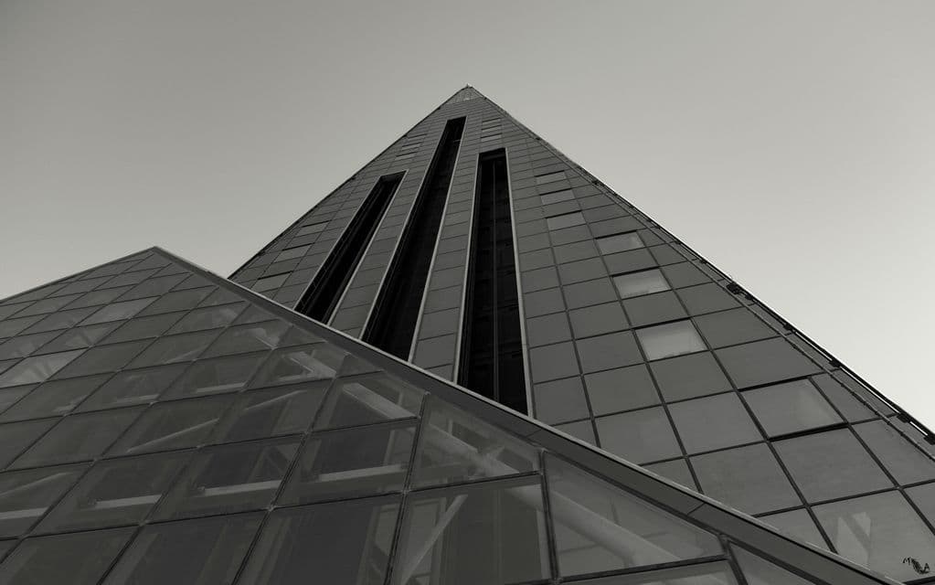 Una toma en contrapicado, en blanco y negro, de un edificio moderno con forma de pirámide y fachada de cristal contra un cielo despejado.