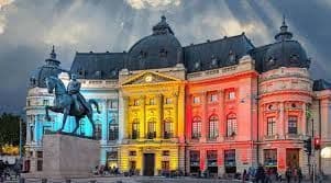 Un edificio storico ornato illuminato con luci blu, gialle e rosse, con una statua equestre su un piedistallo in primo piano.