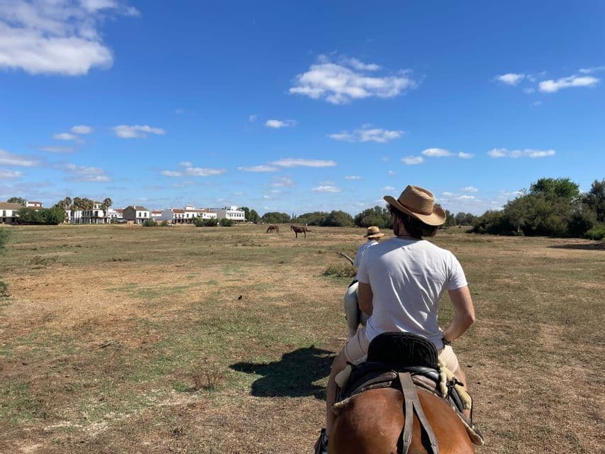 Un viaggio di gruppo WeRoad a cavallo attraverso un campo d'erba secca, verso una cittadina sotto un cielo parzialmente nuvoloso.