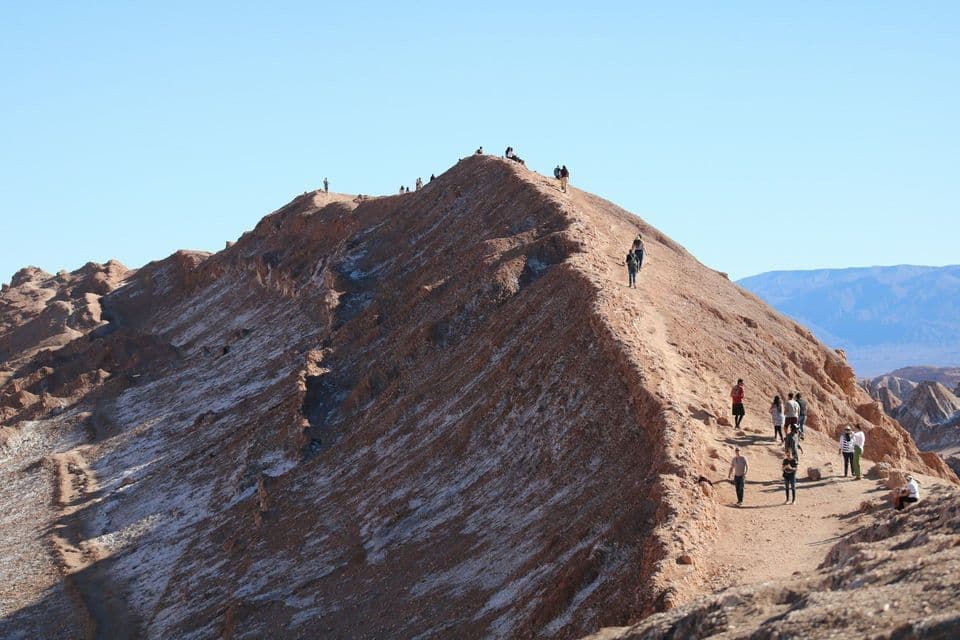 Un viaggio di gruppo WeRoad con escursione lungo la stretta cresta di una grande montagna sabbiosa sotto un cielo sereno.
