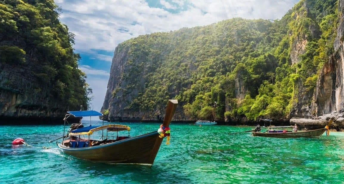 Due tradizionali barche a coda lunga galleggiano su acque turchesi in una laguna tra ripide scogliere boscose.