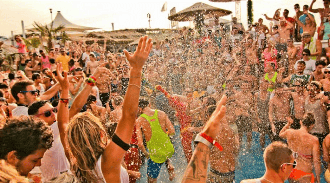 Un viaggio di gruppo WeRoad con persone che ballano tra la folla a una festa in spiaggia, bagnate dagli spruzzi d'acqua.