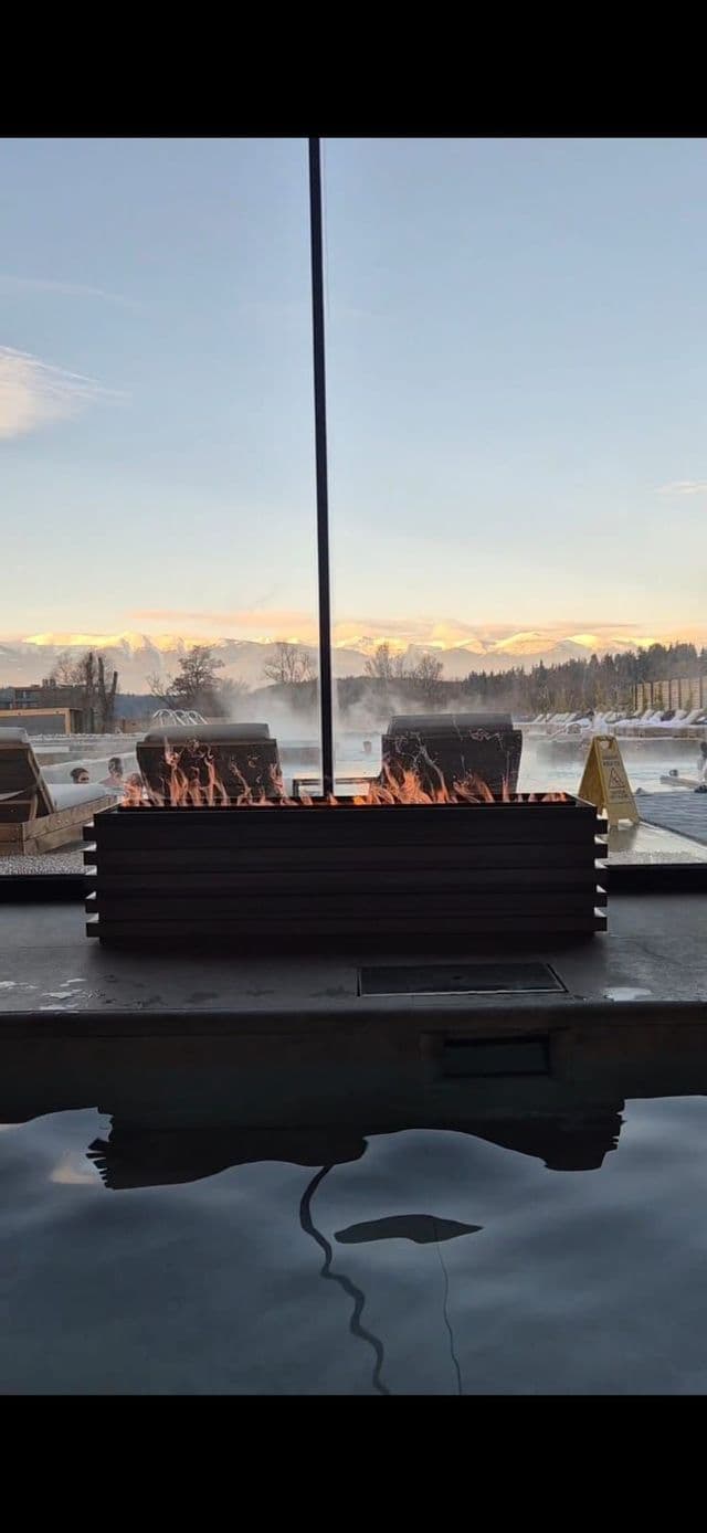 Un viaje en grupo de WeRoad relajándose en una piscina termal al aire libre con una fogata, con vistas a una cordillera nevada al atardecer.
