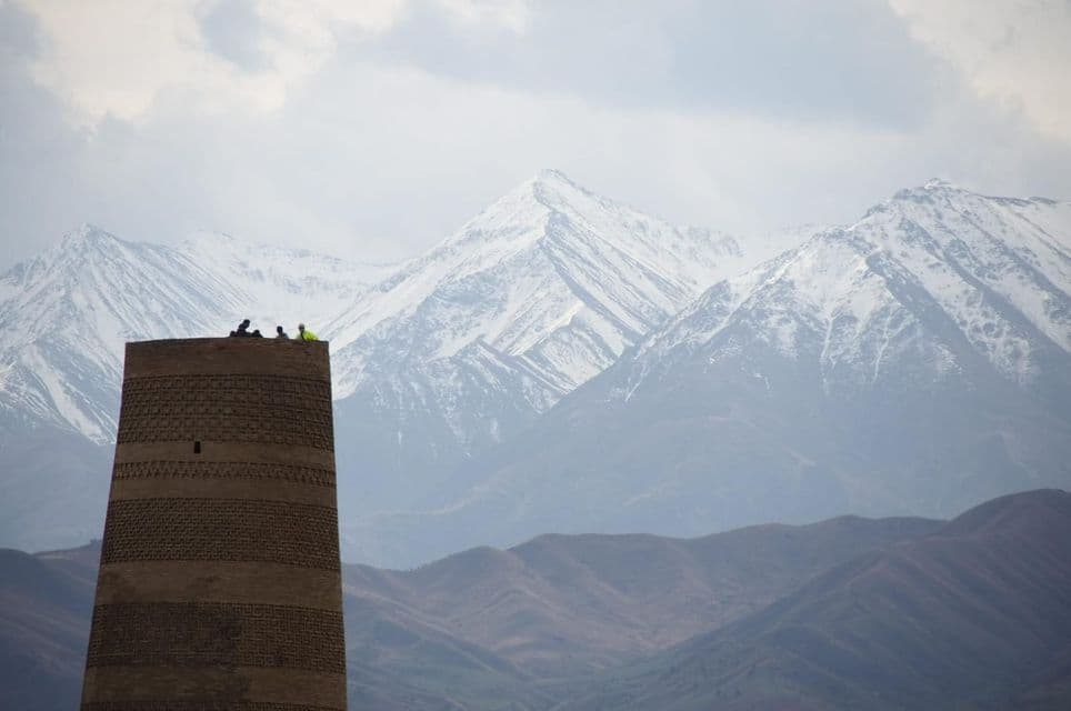 Un gruppo in viaggio WeRoad si staglia su un'alta torre di mattoni, con una vasta catena montuosa innevata sullo sfondo.