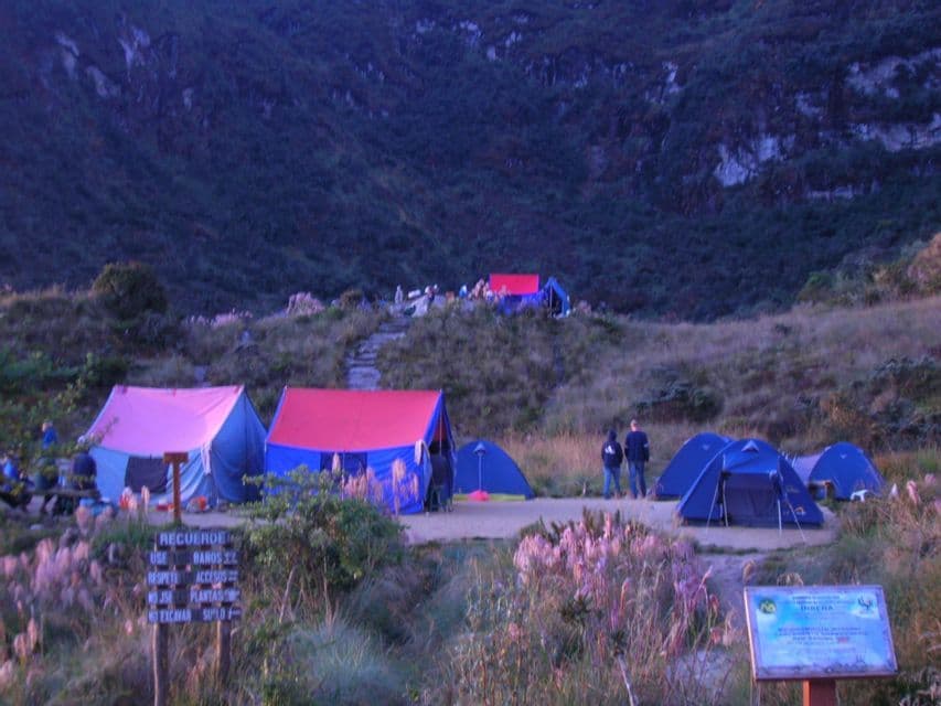 A WeRoad group trip camps in colorful tents in a grassy mountain valley at dusk.