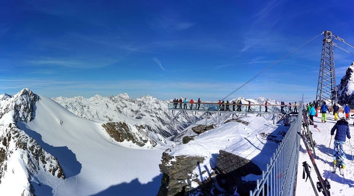 Un groupe WeRoad sur une plateforme panoramique surplombant une chaîne de montagnes enneigée sous un ciel bleu.
