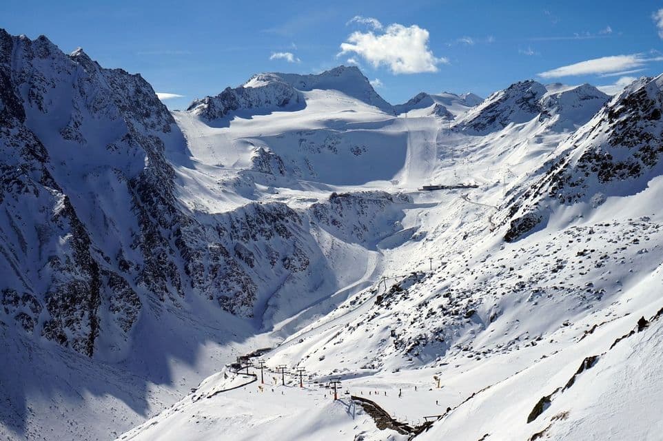 Eine weite, schneebedeckte Berglandschaft mit Skiliften und Pisten, sichtbar unter einem strahlend blauen Himmel mit einigen Wolken.