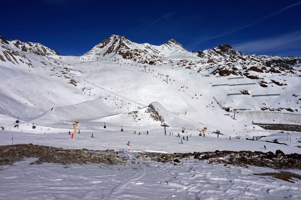 Una vista panoramica di una stazione sciistica in una giornata di sole, con sciatori sulle piste innevate e seggiovie che salgono sulle montagne.