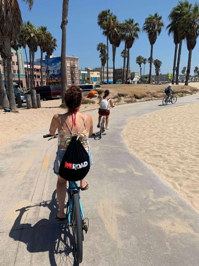 Eine WeRoad-Gruppenreise radelt auf einem befestigten Weg entlang eines palmengesäumten Sandstrandes.