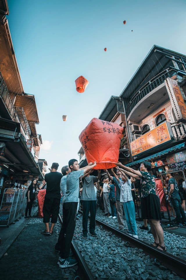 Una vista dal basso di un gruppo di persone che rilasciano lanterne di carta rosse dai binari del treno in una via stretta.