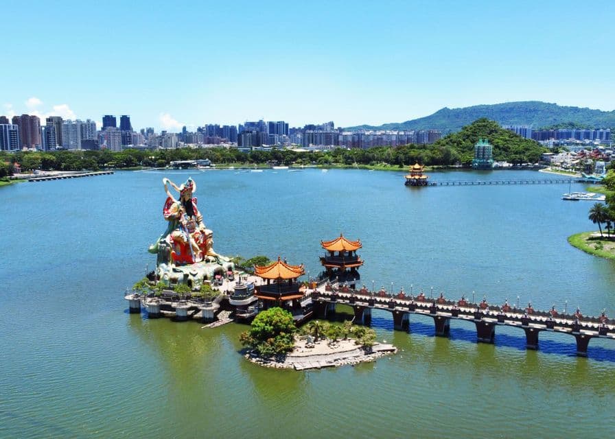 Una vista aerea di una grande statua colorata e pagode tradizionali su isole all'interno di un lago, con uno skyline della città sullo sfondo.