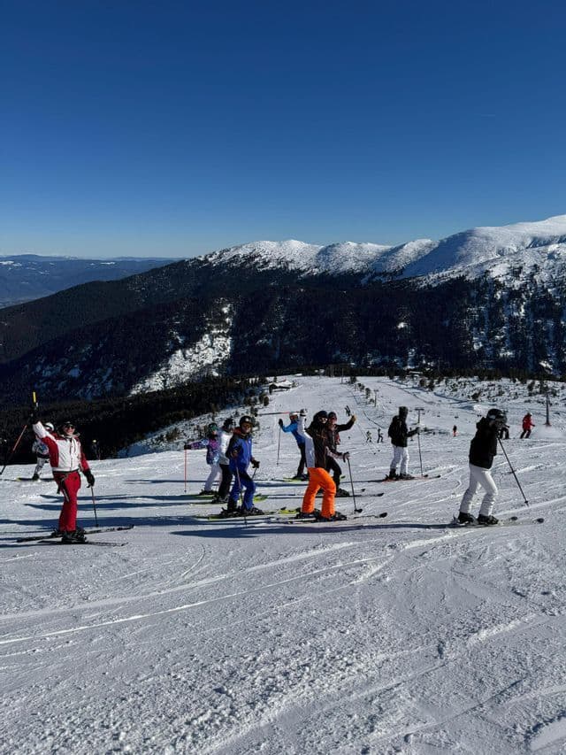 Un groupe WeRoad posant à ski sur une pente de montagne enneigée et ensoleillée, sous un ciel bleu clair.