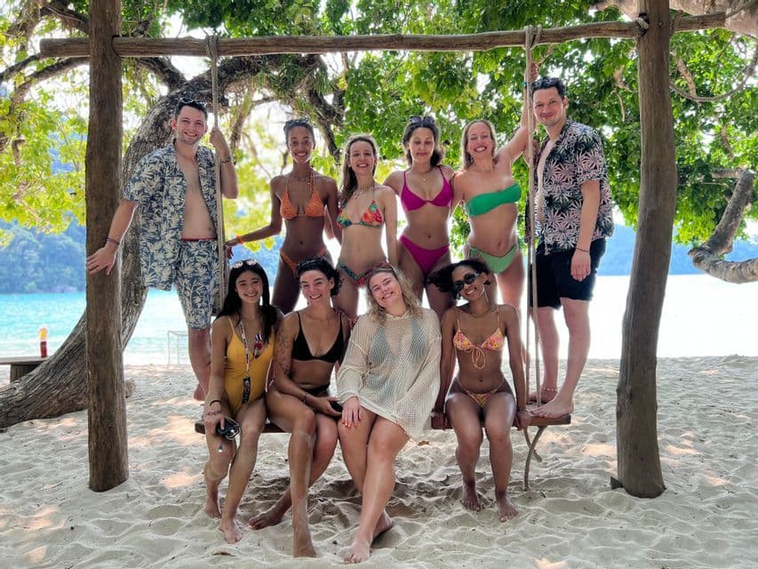 Un viaggio di gruppo WeRoad in posa per una foto su una grande altalena di legno su una spiaggia sabbiosa, con il mare sullo sfondo.
