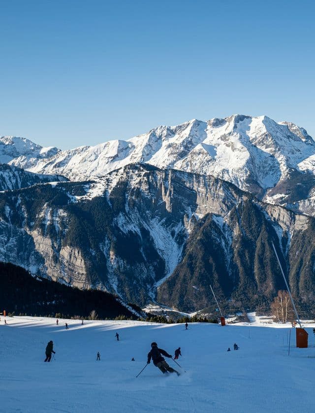 Sciatori scendono un pendio innevato in una giornata di sole, con grandi montagne innevate sotto un cielo limpido.