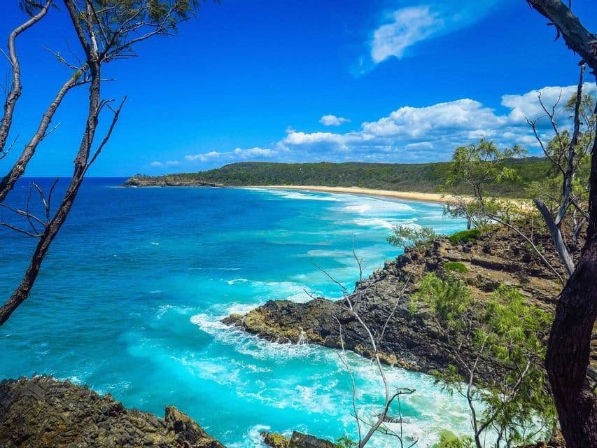 Ein Blick von einem hohen Aussichtspunkt auf eine tropische Küste mit türkisfarbenem Wasser, einem Sandstrand und grünen Hügeln.