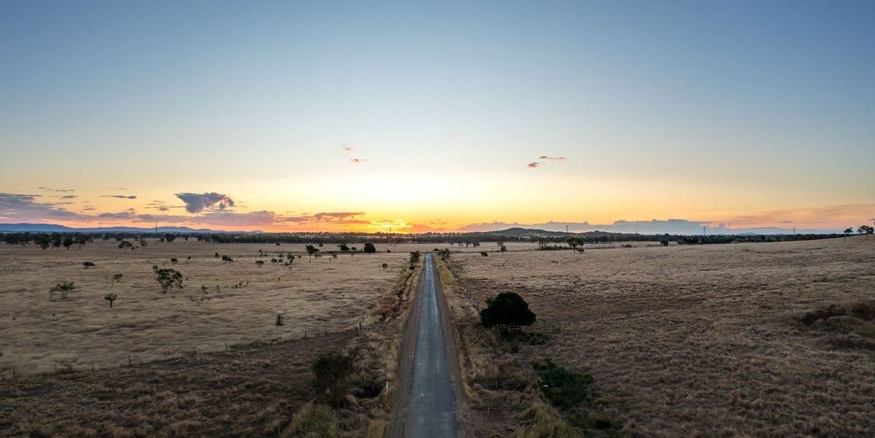 Una vista aerea di una strada dritta che si estende attraverso una vasta savana secca verso il sole che tramonta all'orizzonte.