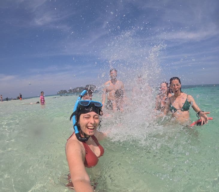 Eine WeRoad-Gruppenreise plantscht im klaren Meer, während eine Frau mit Schnorchelmaske ein lächelndes Selfie macht.