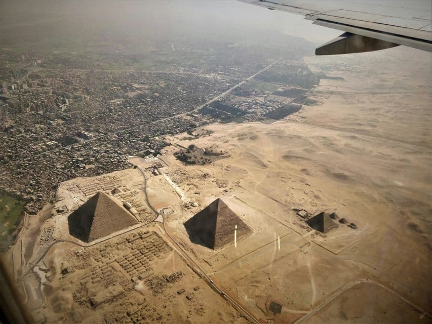 Vue aérienne depuis un avion montrant les pyramides de Gizeh à la frontière entre une vaste ville et le désert.