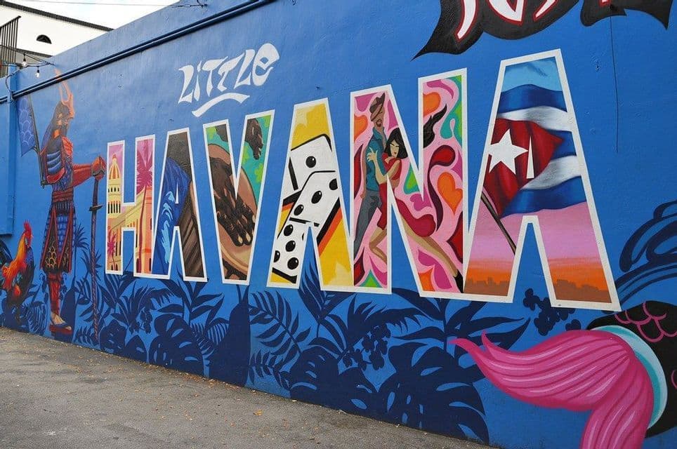 Un murale colorato su una parete blu recita 'Little Havana'. Le lettere mostrano icone culturali cubane come domino, ballerini e la bandiera.