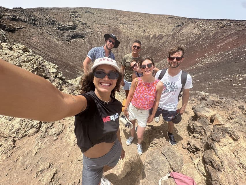 Un groupe WeRoad prend un selfie sur le bord rocheux d'un grand cratère sous un ciel clair.