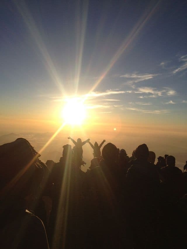 Un viaggio di gruppo WeRoad in silhouette contro una splendida alba dalla cima di una montagna, con due persone che alzano le braccia.