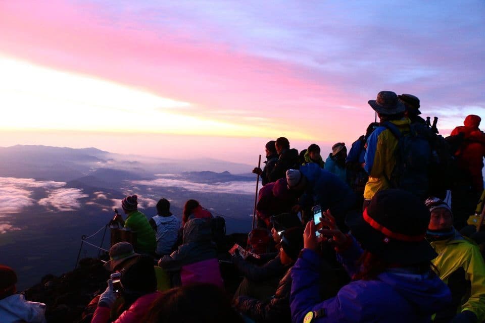 Un viaggio di gruppo WeRoad osserva un'alba colorata da una cima di montagna, affacciandosi su un mare di nuvole e montagne lontane.