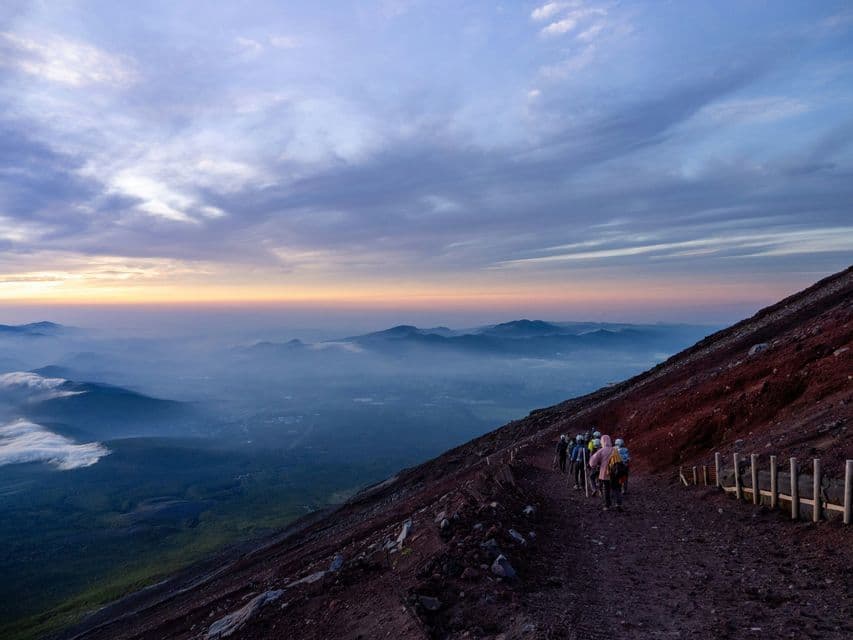 Un viaggio di gruppo WeRoad percorre un ripido sentiero di montagna che si affaccia su una valle nebbiosa all'alba.