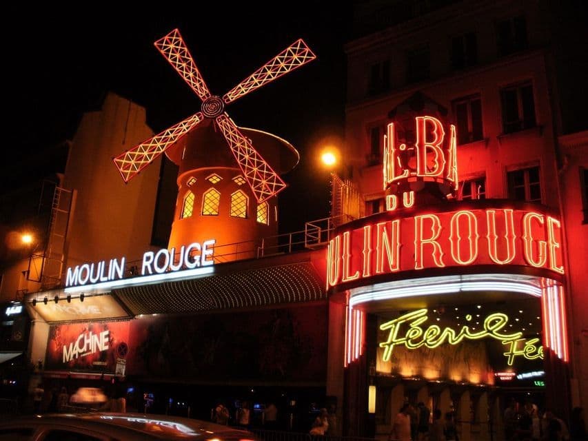 Le bâtiment du cabaret du Moulin Rouge la nuit, avec son iconique moulin rouge et son entrée illuminés par des néons rouges vifs.