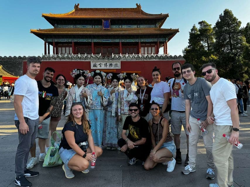 Un groupe WeRoad posant pour une photo avec des femmes locales en costumes traditionnels devant une porte historique rouge.