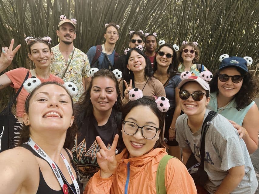 Un groupe WeRoad souriant pour un selfie dans une forêt de bambous, avec de nombreuses personnes portant des serre-têtes oreilles de panda.