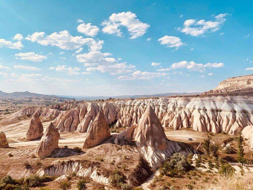Un vasto paesaggio di formazioni rocciose coniche in una valle arida sotto un cielo azzurro brillante con nuvole.