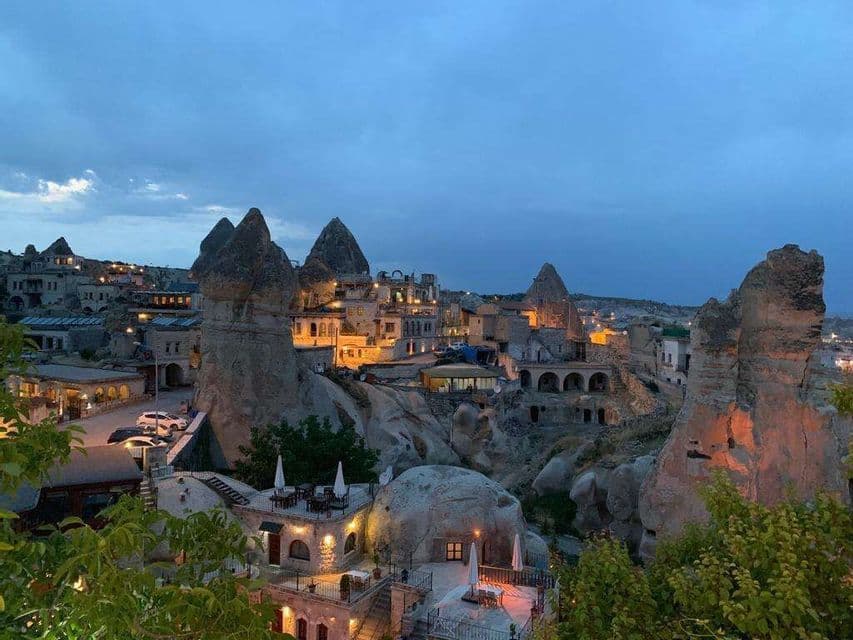 Un pueblo construido en formaciones rocosas distintivas, iluminado por luces cálidas bajo un cielo azul al atardecer.