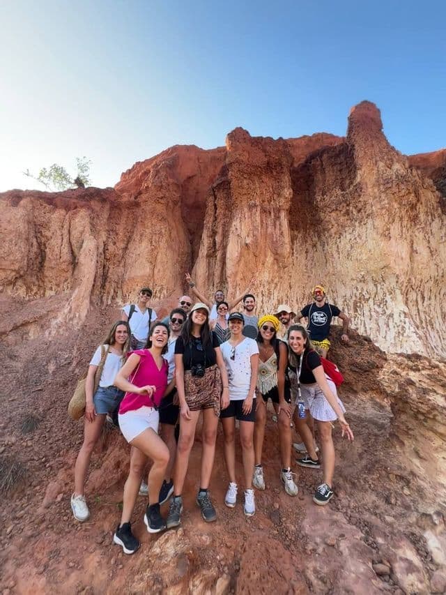 Un gruppo WeRoad sorride per una foto mentre si trova su un sentiero roccioso di fronte a un canyon di roccia rossa.