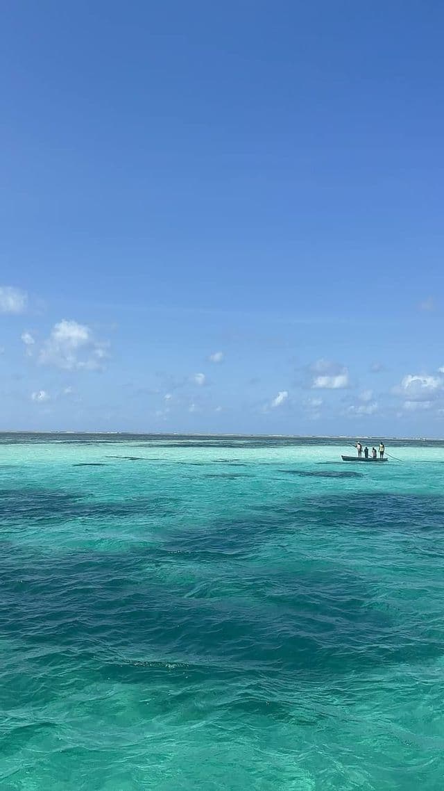 Un viaggio di gruppo WeRoad su una piccola barca che galleggia su un vasto oceano turchese, sotto un cielo azzurro limpido con nuvole leggere.