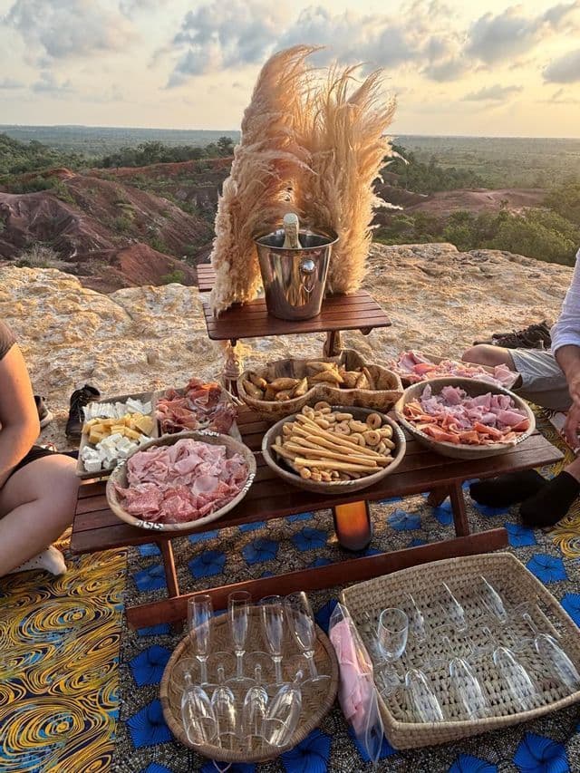 Un picnic all'aperto con spumante, salumi e formaggi su un tavolo di legno con vista su un canyon al tramonto.