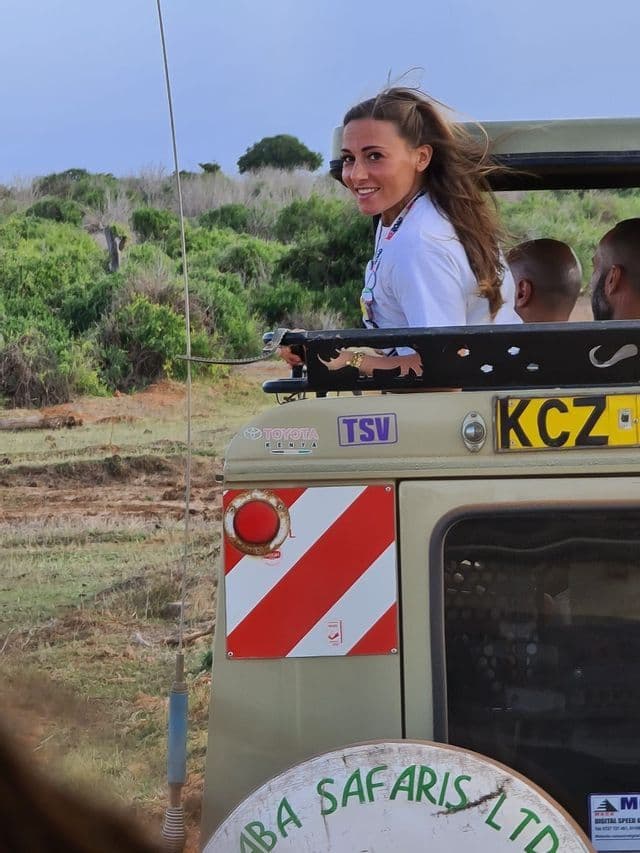 Una donna in un viaggio di gruppo WeRoad sorride guardando indietro da un veicolo safari scoperto in una savana.
