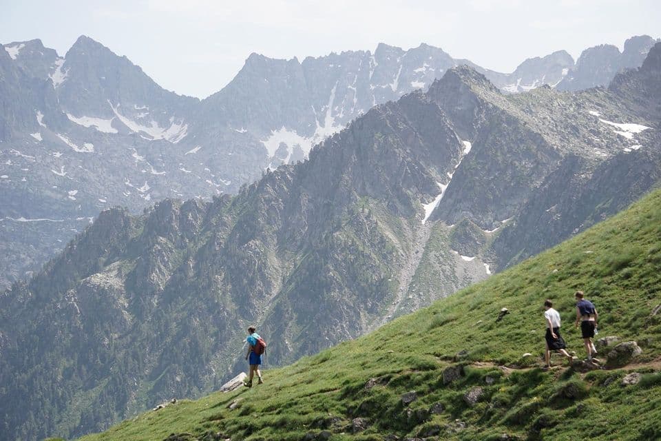 Viaje en grupo de WeRoad haciendo senderismo por una ladera empinada y cubierta de hierba, con un telón de fondo de picos rocosos y nevados.