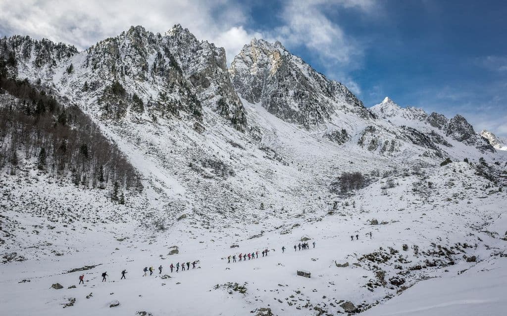 Un viaje en grupo de WeRoad haciendo senderismo en fila por un paisaje nevado con grandes montañas rocosas al fondo.