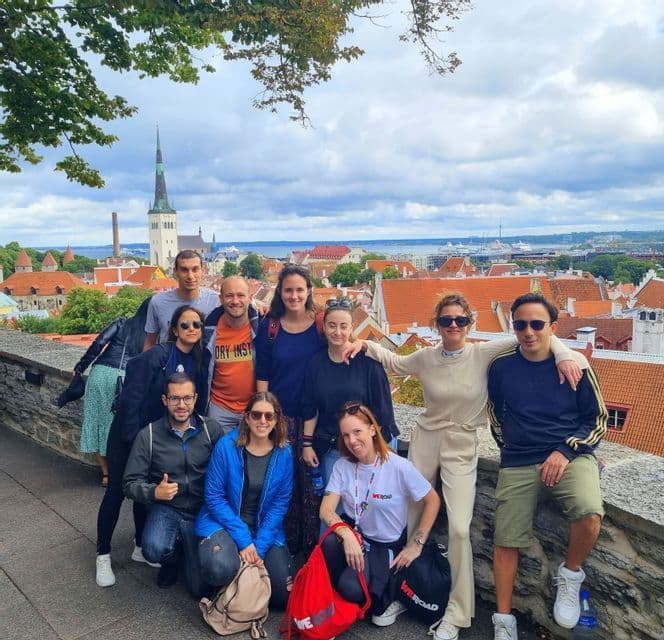 Eine WeRoad-Gruppenreise posiert für ein Foto auf einem steinernen Aussichtspunkt mit Blick auf eine Stadt mit roten Ziegeldächern und einem Kirchturm.