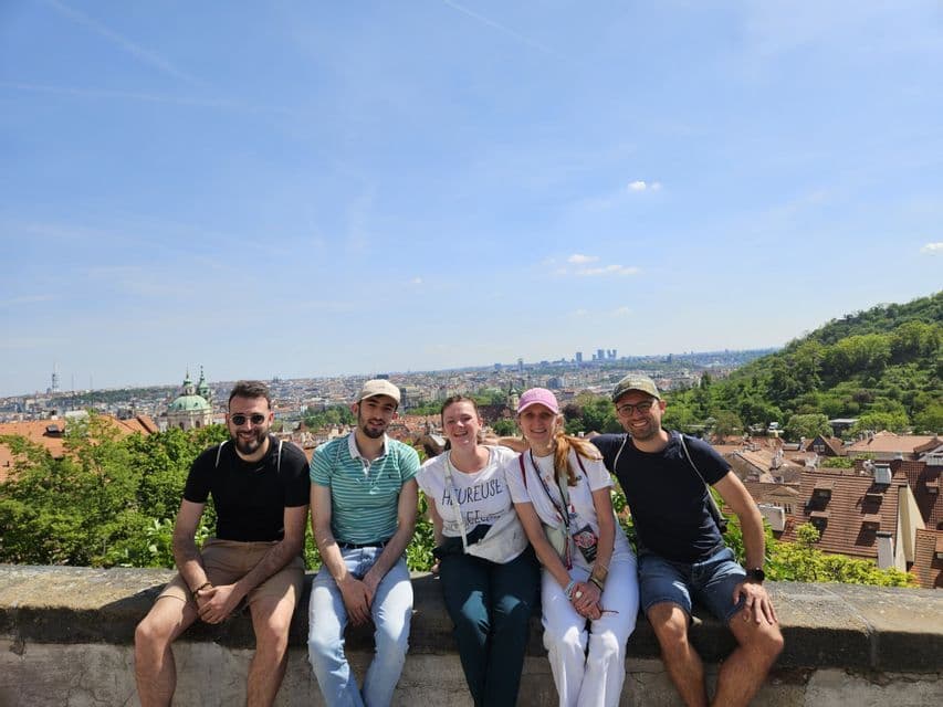 Un voyage de groupe WeRoad de cinq personnes assises sur un mur en pierre et souriantes, avec une vue panoramique sur la ville en arrière-plan.