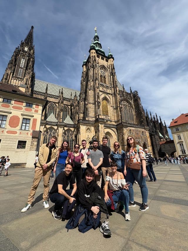 Un groupe WeRoad pose pour une photo sur une grande place devant une cathédrale gothique ornée sous un ciel bleu.
