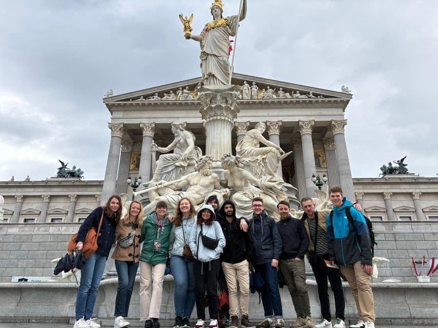 Un voyage de groupe WeRoad posant pour une photo devant une grande fontaine en marbre et un bâtiment néoclassique sous un ciel couvert.