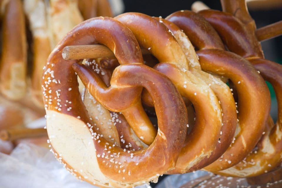 A close-up of large, soft pretzels sprinkled with coarse salt hanging on a wooden display stand.