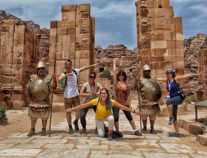 Eine WeRoad Gruppenreise posiert mit zwei als antike Soldaten verkleideten Personen vor Steinruinen.