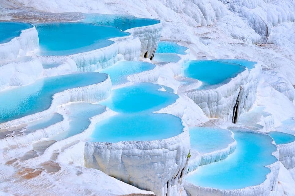 Terraced pools of bright blue water cascade down white mineral deposits, creating a layered landscape.